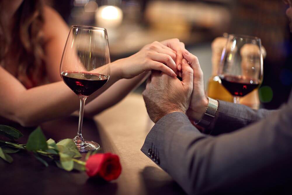 女性の手を握る男性の画像。テーブルにはワイングラスと赤いバラが一輪。店外で会おうとしてくる客の中にもロマンチストはいるのかも。
