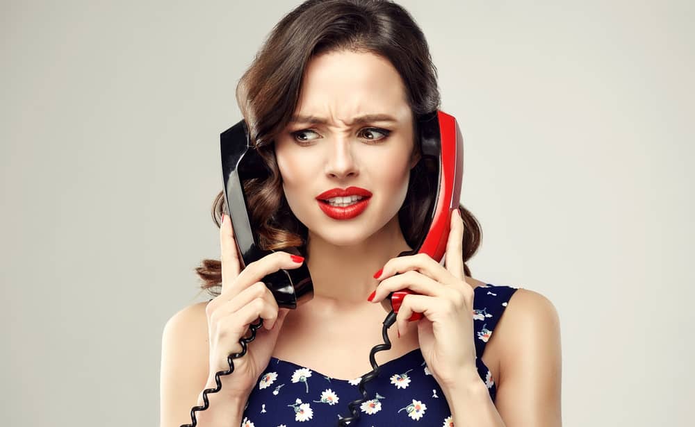 ２つの固定電話で同時に会話する。しかめっ面の女性の画像。